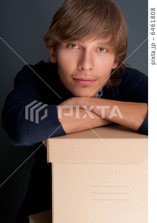 Portrait of young man holding on box against grey wall. He is st Portrait of young man holding on box against grey wall. He is st 6461808
