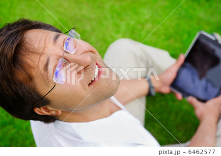 Adult man sitting on grass and using his tablet computer 6462577