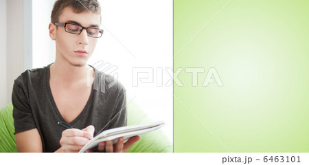 Young adult man writing in his copybook while sitting on a large Young adult man writing in his copybook while sitting on a large 6463101