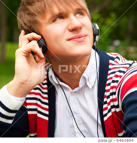 Student outside sitting on green grass and listening music via h 6463804