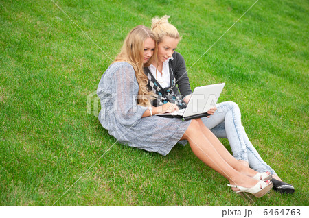 Portrait of two smiling women using laptop on a green meadow at Portrait of two smiling women using laptop on a green meadow at 6464763