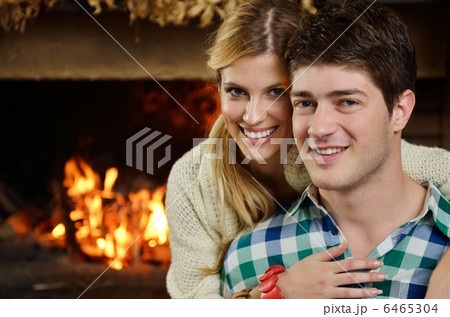 Young romantic couple sitting on sofa in front of fireplace at h 6465304