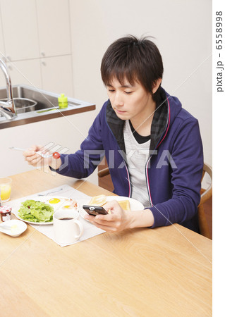 携帯を見ながら朝食を食べる男性 6558998