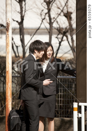 バス亭で時刻表を見るスーツ姿の若い男女 6559379