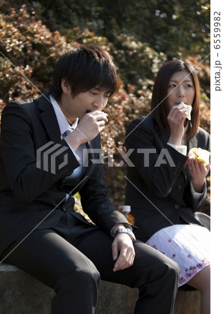 公園で昼食を食べるスーツ姿の若い男女 6559982