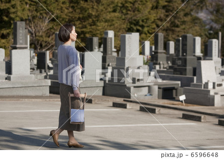 花と水桶を持ち墓地を歩く女性 6596648