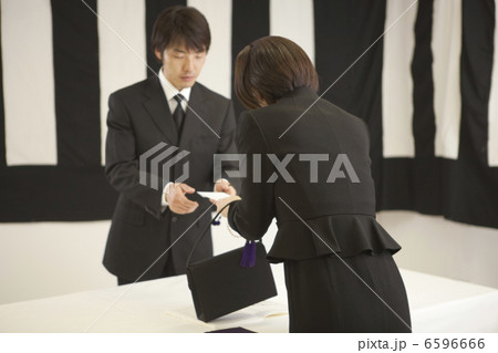 香典袋を手渡す喪服姿の女性と受付の男性 6596666