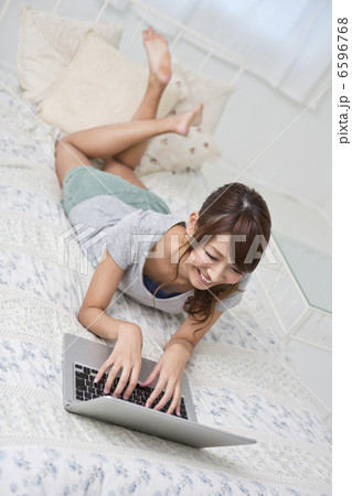 ベッドの上でノートＰＣを操作する若い女性 6596768