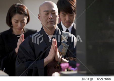 お墓の前で手を合わせる僧侶と喪服姿の遺族 6597000