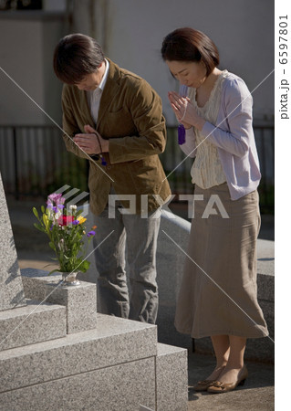 お墓の前で手を合わせる夫婦 6597801