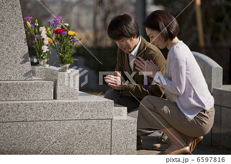 お墓の前で手を合わせる夫婦 6597816
