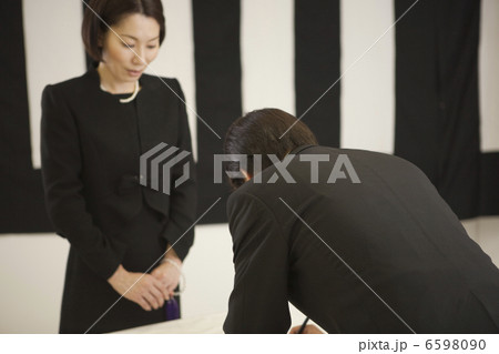 記帳をする喪服姿の男性と受付の女性 6598090