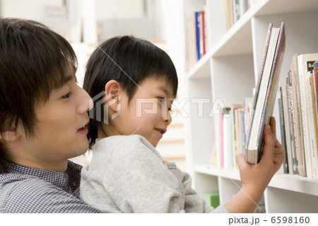 父に抱えられて本をとる息子 6598160
