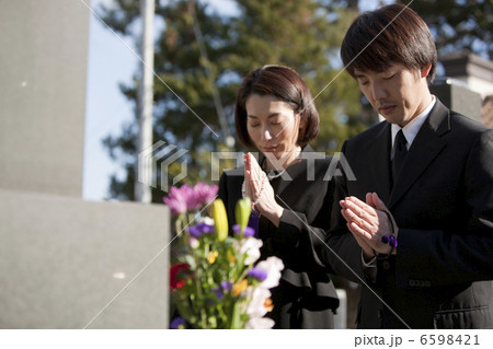 お墓の前で手を合わせる喪服姿の夫婦 6598421