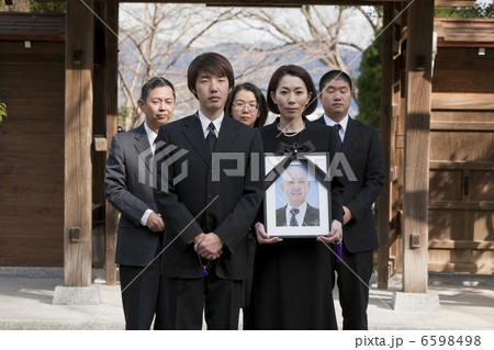 遺影を持って山門の前に立つ女性と遺族 6598498