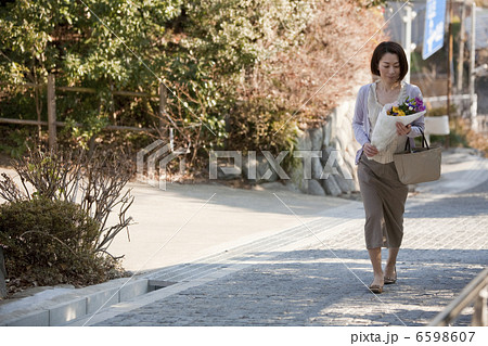 坂を上りお墓参りに向かう花を持った女性 6598607