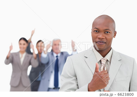 Businessman with cheering team behind him giving thumb up Businessman with cheering team behind him giving thumb up 6623800