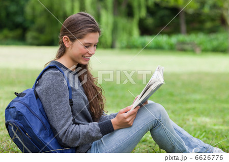 Young relaxed woman sitting on the grass while reading a book 6626776