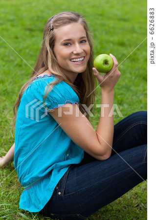 Smiling young woman holding a green apple while sitting in a par Smiling young woman holding a green apple while sitting in a par 6626883