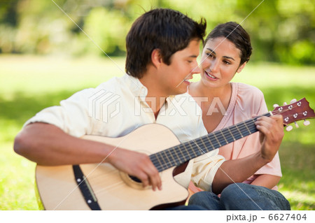 Man playing the guitar while his friend watches him 6627404