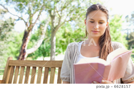 Woman sitting on a park bench while reading a book 6628157