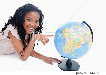 A young girl smiling at the camera has her finger on a globe 6629098