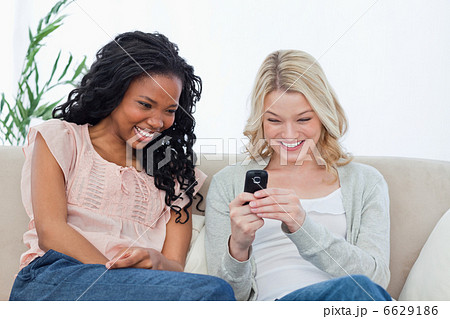 A woman holding a mobile phone is sitting on a couch with her fr 6629186