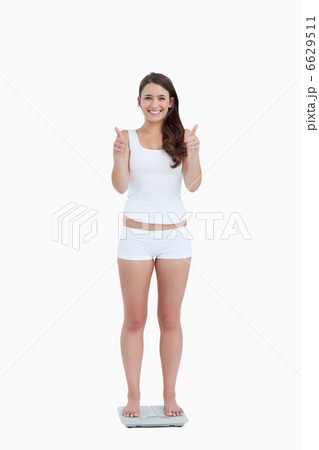 Smiling woman placing her thumbs up while standing on weighing s Smiling woman placing her thumbs up while standing on weighing s 6629511