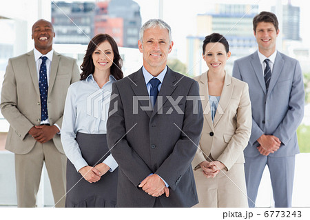 Mature smiling manager standing upright and followed by his team Mature smiling manager standing upright and followed by his team 6773243