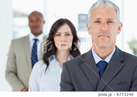 Mature and serious manager standing upright and followed by two Mature and serious manager standing upright and followed by two 6773246