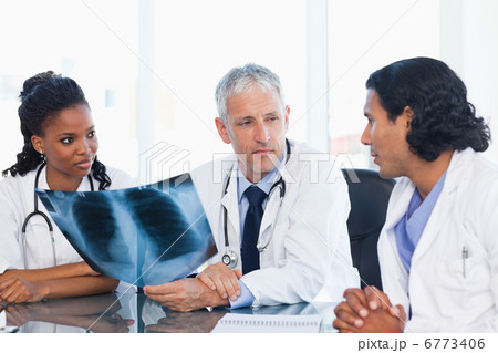 Mature doctor looking at an x-ray with two members of his team Mature doctor looking at an x-ray with two members of his team 6773406