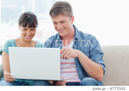 A pretty couple sitting while using a laptop together A pretty couple sitting while using a laptop together 6773502