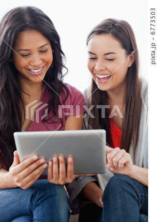 Close up half length shot of two laughing women looking at a tab 6773503
