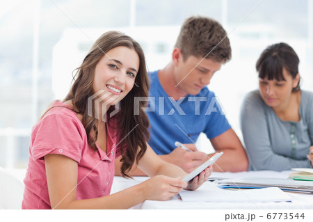 A brightly smiling girl with friends as she uses a tablet 6773544