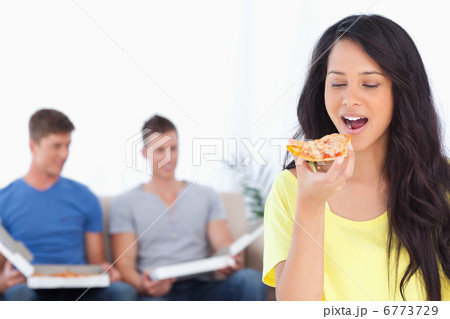 Woman about to eat a pizza slice as her friends sit behind her 6773729