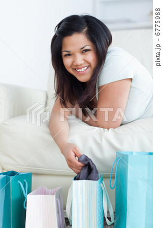Woman on a couch holding clothes up from a shopping bag 6775988