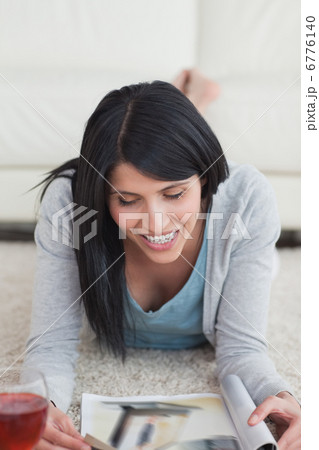 Woman smiling while lying on the floor and reading a magazine Woman smiling while lying on the floor and reading a magazine 6776140