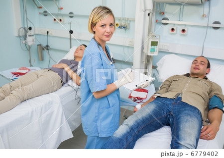 Two patients lying on bed next to a nurse 6779402
