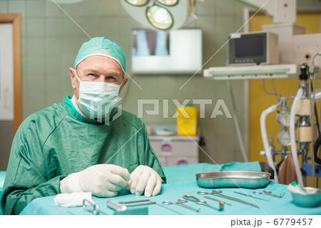 Surgeon sitting next to a table full of a surgical tools Surgeon sitting next to a table full of a surgical tools 6779457