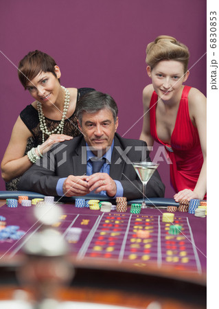 Women standing with man at roulette table Women standing with man at roulette table 6830853