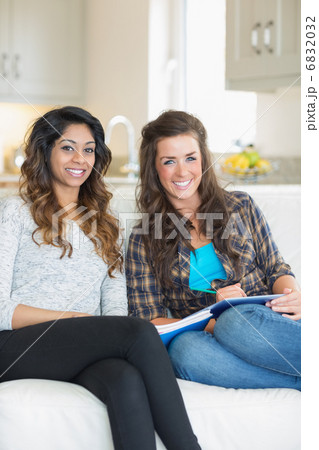 Two smiling girls sitting on a couch while writing on a notepad 6832032