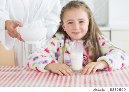 Happy little girl with glass of milk getting cereal from her mot 6832690