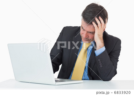 Troubled man sitting at his desk with a laptop 6833920
