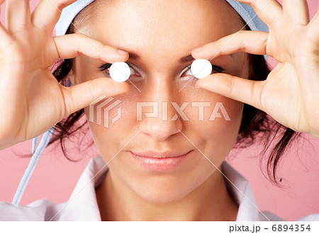Closeup portrait of young nurse showing pills over eyes Closeup portrait of young nurse showing pills over eyes 6894354