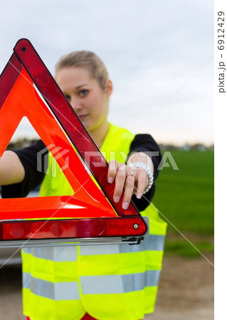 Young woman with warning triangle on street Young woman with warning triangle on street 6912429