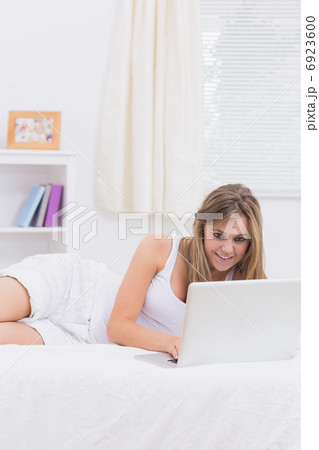 Cheerful woman lying on her bed with a laptop Cheerful woman lying on her bed with a laptop 6923600