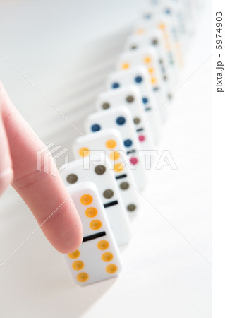 Finger about to knock over line of dominoes 6974903