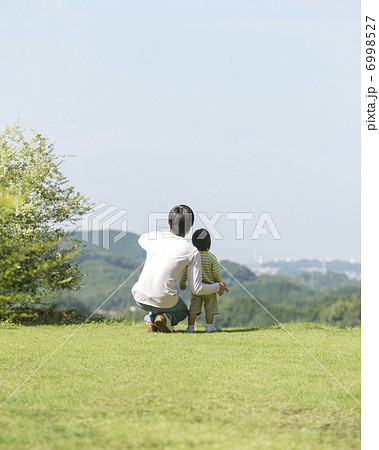 草原にしゃがむ父と子の後ろ姿の写真素材