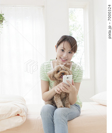 A Woman Sitting On A Bed With A Toy Poodle On Stock Photo