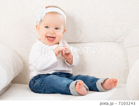 happy little baby girl laughing and sitting on a sofa in jeans 7103243